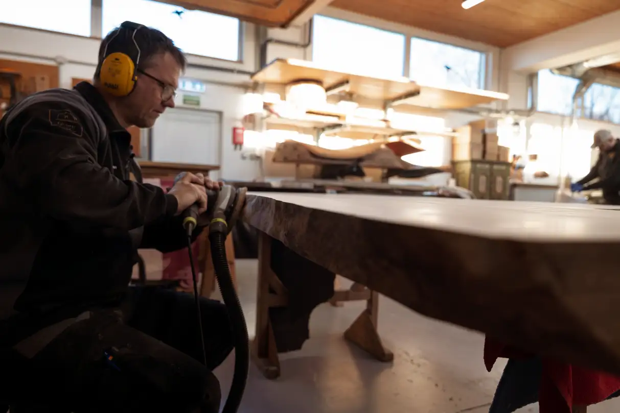 Sanding a solid wood live edge table in the workshop – handcrafted natural wood furniture
