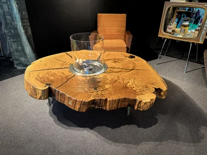 Tavolino in quercia con bordo naturale ricavato da una fetta di tronco, accanto a una moderna poltrona