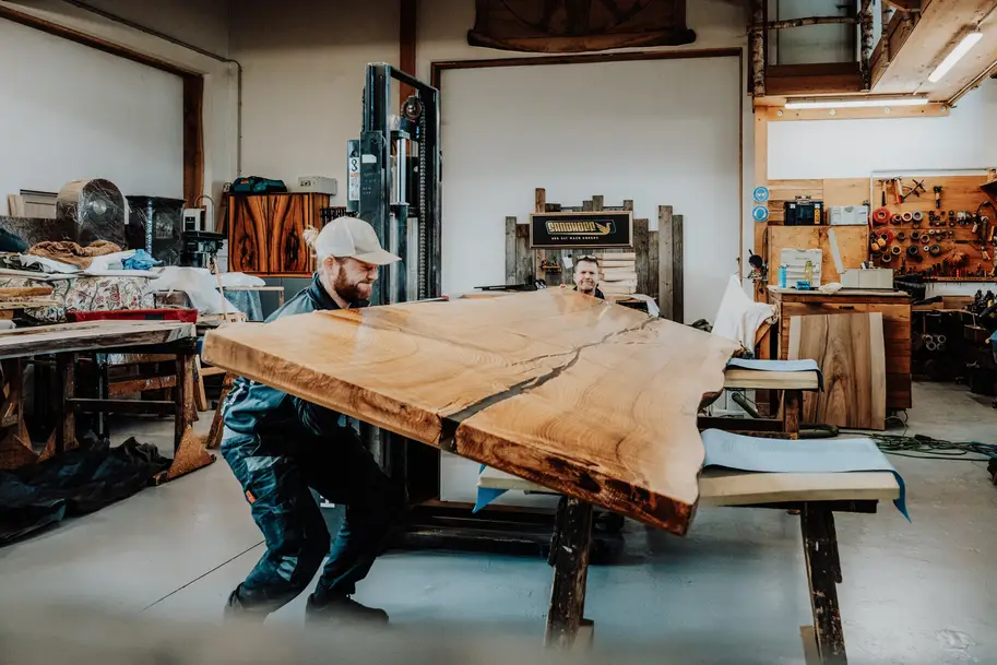 Due falegnami girano un pesante piano in legno massiccio per la lavorazione