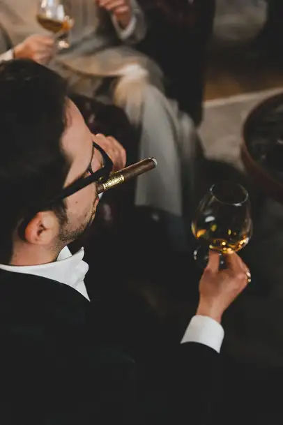 L'uomo tira una boccata da un sigaro e tiene un bicchiere di rum