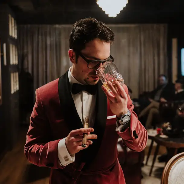 Uomo in abito rosso tiene un sigaro e annusa un bicchiere di rum