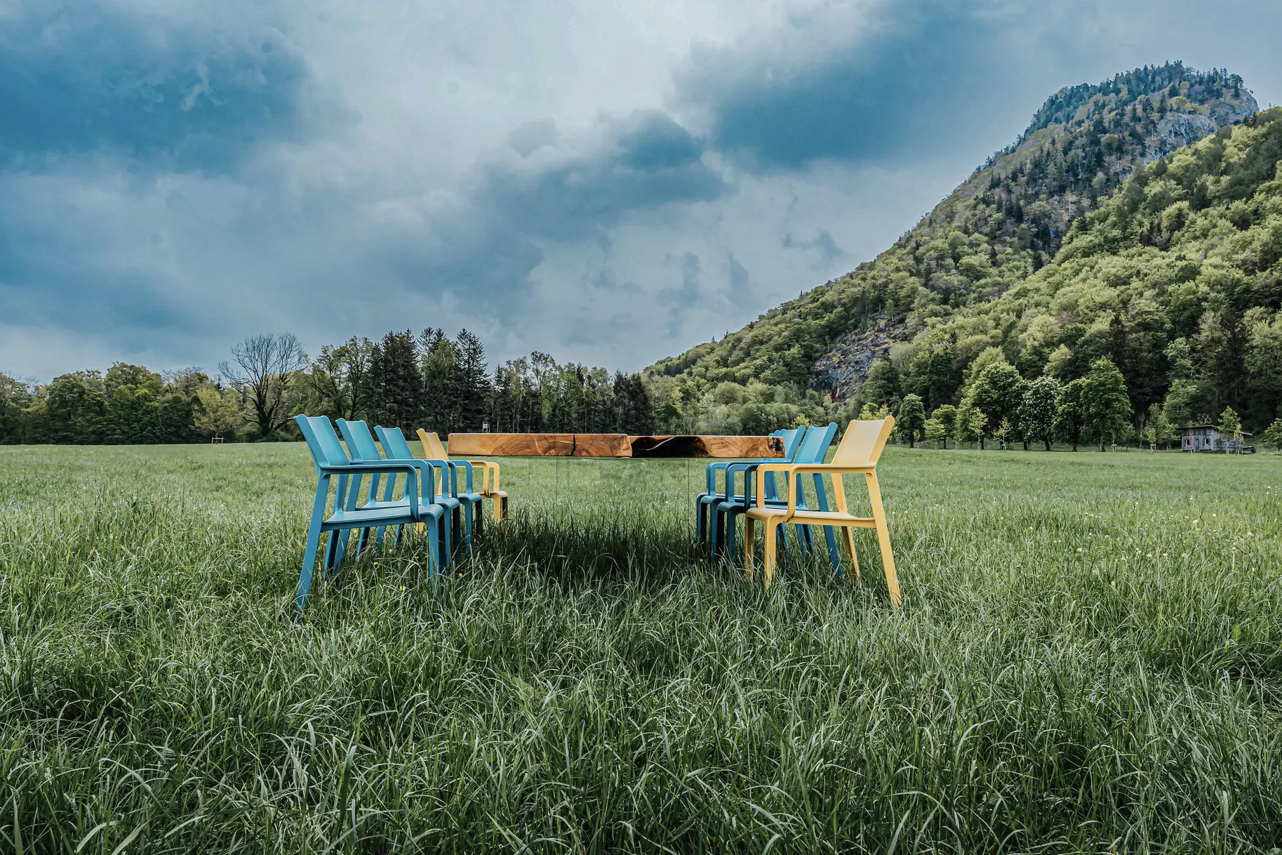 Mesa de Stammdesign de un tronco con patas de vidrio, que parece flotar, en un prado