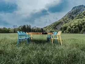 Mesa de Stammdesign de un tronco con patas de vidrio, que parece flotar, en un prado