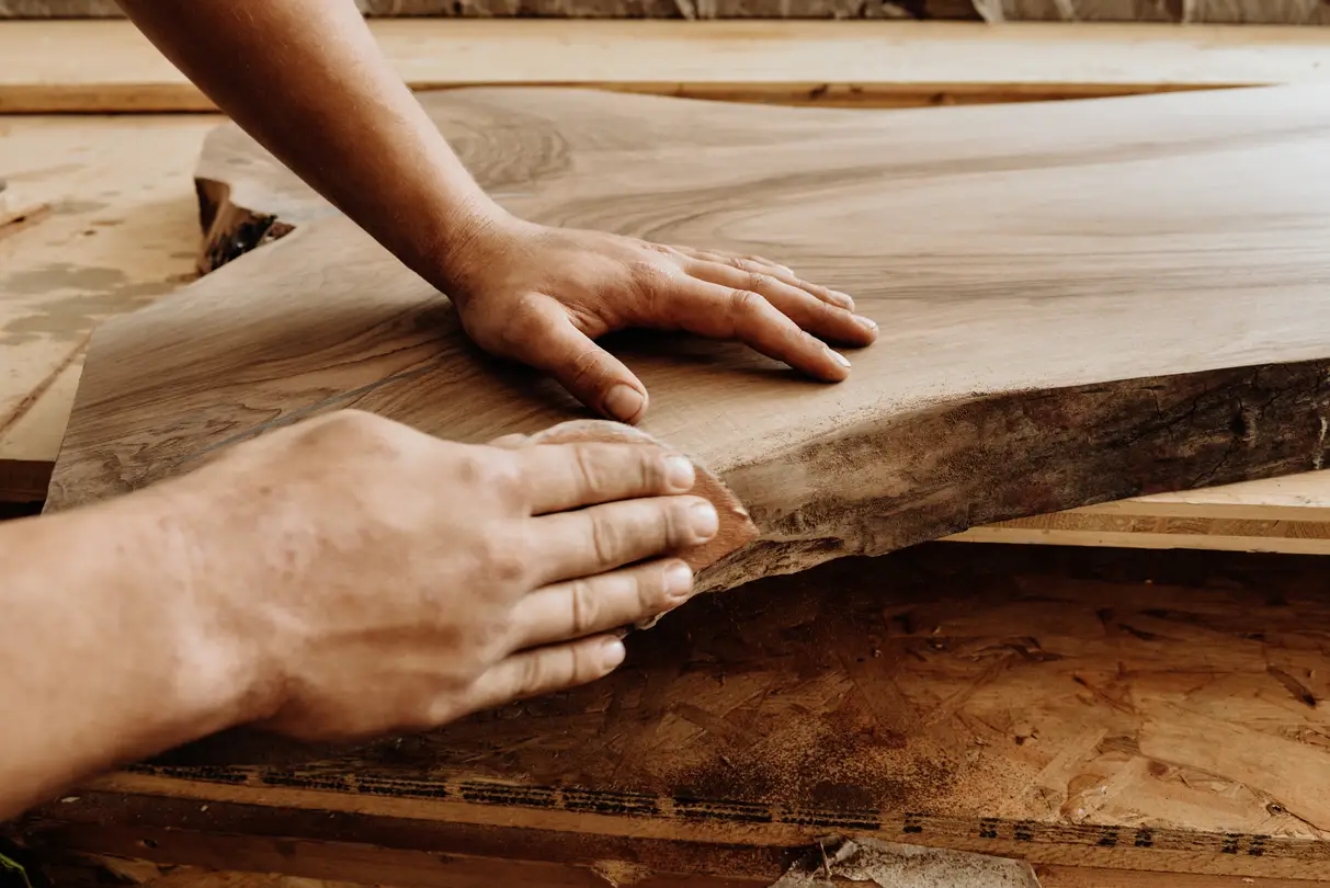 Mani che levigano una lastra di tronco – Lavoro di precisione nella manifattura di tavoli