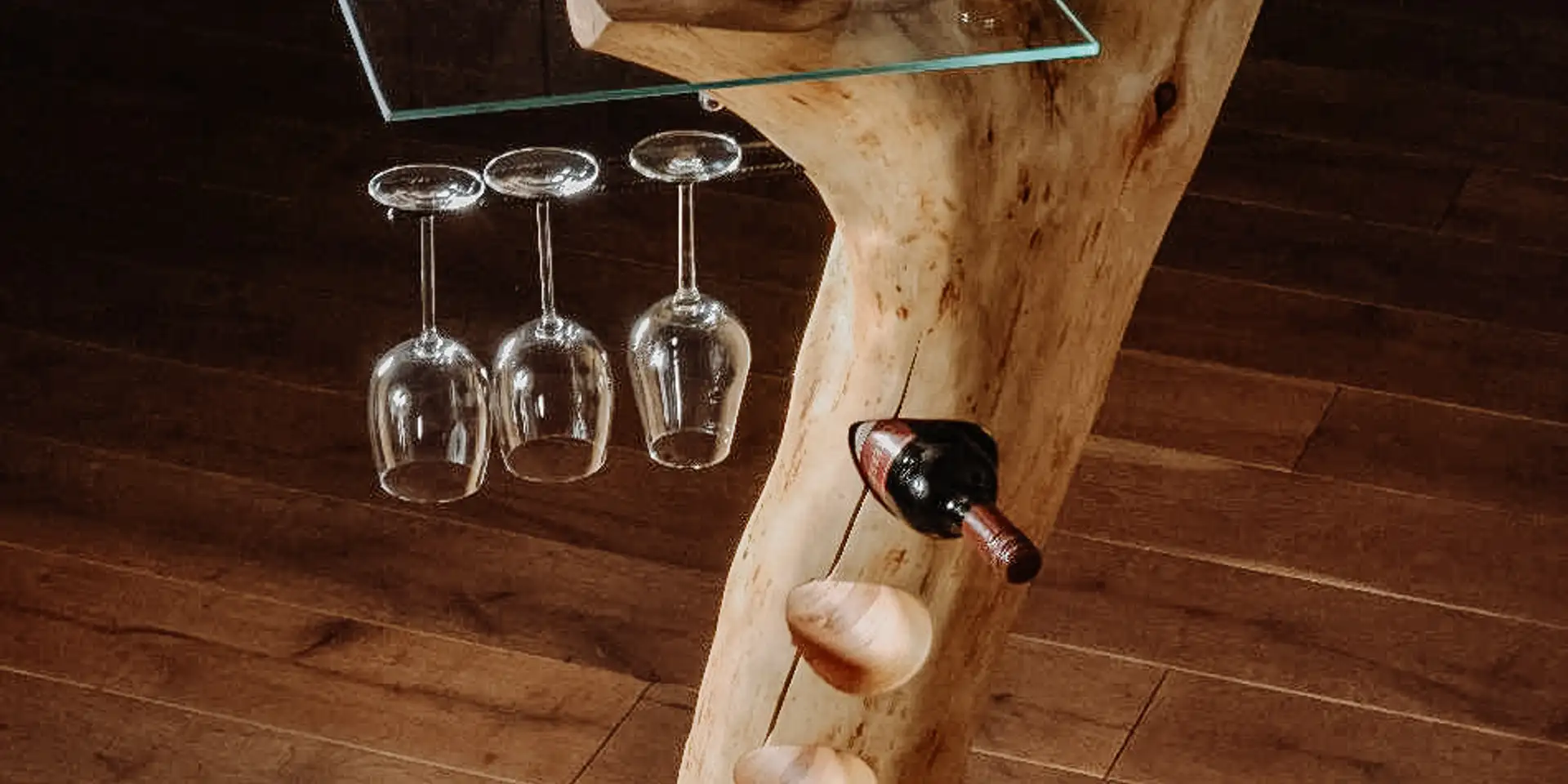 Barra de pie de alta calidad hecha de un tronco de árbol con soporte para botellas y copas de vino, y una resistente superficie de vidrio.