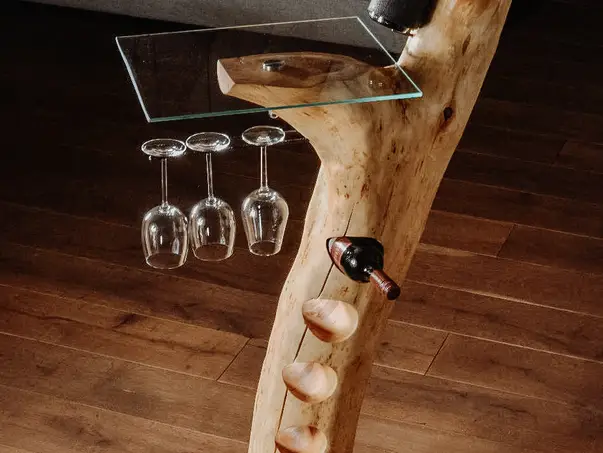 Barra de pie de alta calidad hecha de un tronco de árbol con soporte para botellas y copas de vino, y una resistente superficie de vidrio.