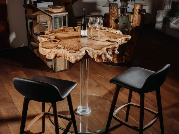 Mesa alta de diseño hecha de una rodaja de árbol de madera maciza con base de vidrio estable para gastronomía y bares.