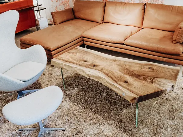 Mesa de café de diseñador hecha de un tronco con superficie exclusiva y patas de vidrio de nogal resistentes.