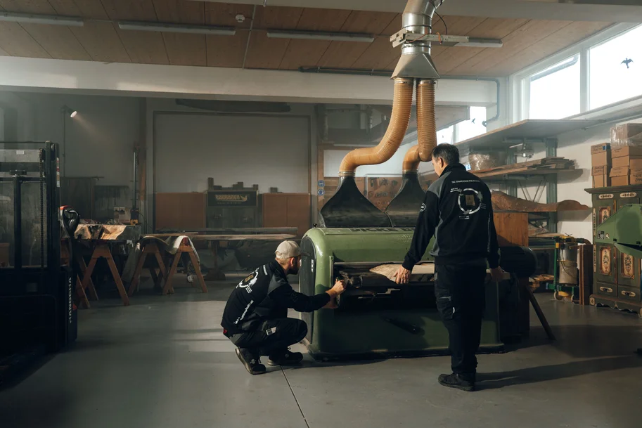 Due collaboratori lavorano una tavola di legno su una macchina di lavorazione nel laboratorio di Stammdesign