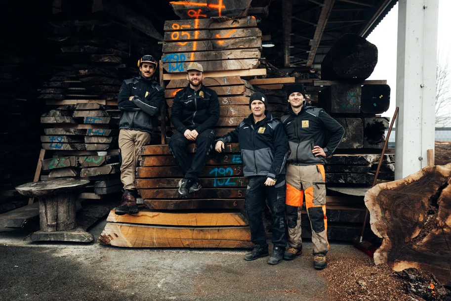 Il team di Stammdesign posa insieme su tronchi d'albero impilati nel deposito
