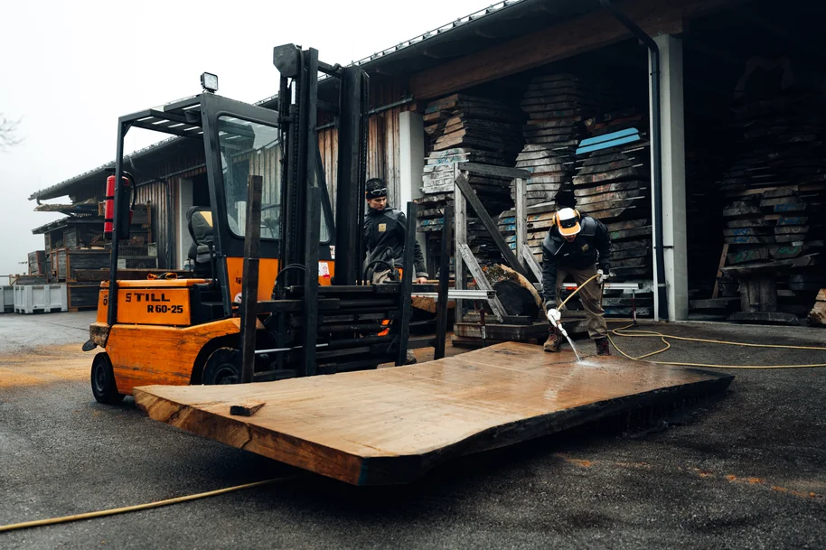 Un collaboratore in abbigliamento da lavoro pulisce una tavola di legno con un tubo dell'acqua all'esterno della manifattura