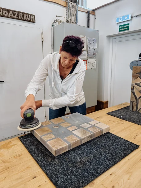 Kursteilnehmerin schleift ein Schneidebrett aus Holz und Epoxidharz