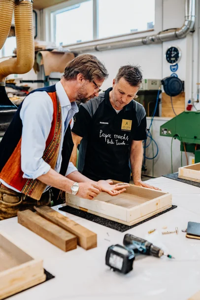 Mann zeigt einem Stammdesign-Mitarbeiter ein Holzstück beim Schneidebrettkurs
